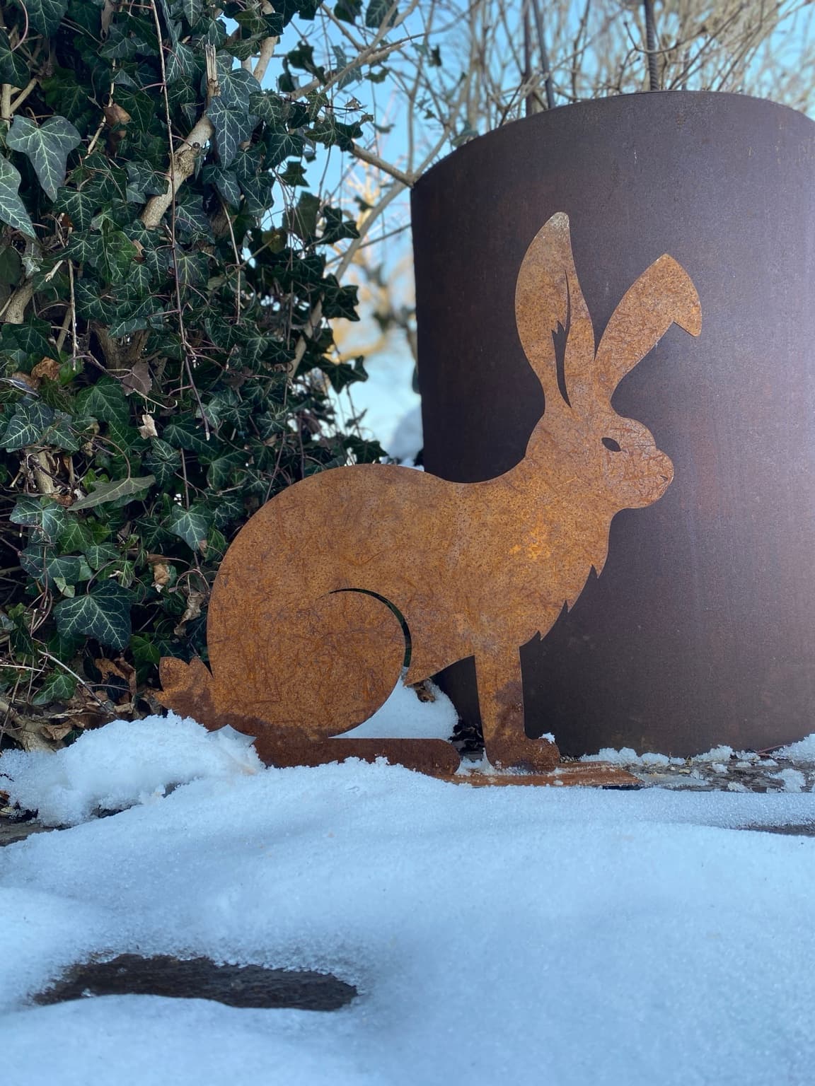 Edelrost-Hase zwischen Efeu und Schnee im Wintergarten
